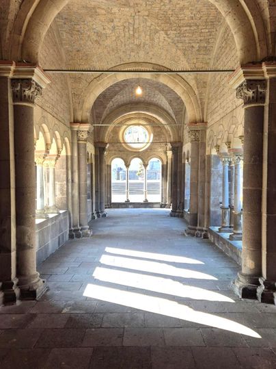 Ein historischer Kreuzgang mit hohen Bögen und Säulen. Das Licht fällt sanft auf den Steinboden und durch die Fenster.