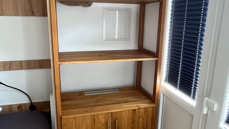 A modern wooden shelf with open shelves and a drawer. Towels are neatly arranged on the top shelf.