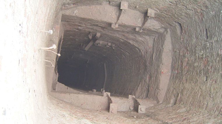 A deep well with calm, stony walls. The view leads into the darkness of the shaft.