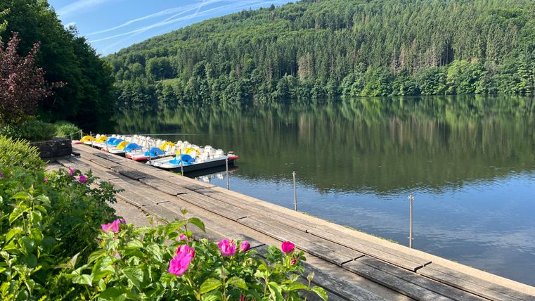 Pedal boats on a jetty on a quiet reservoir with wooded hills in the background.