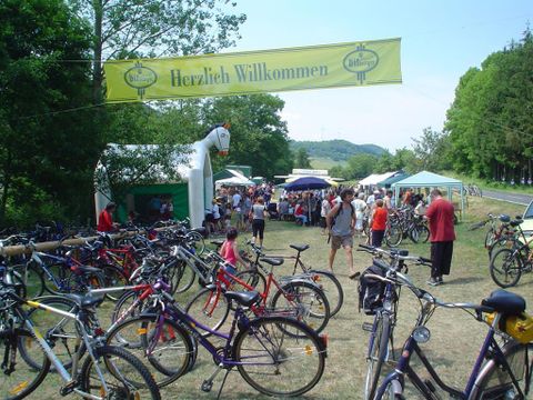 A lively festival with many bicycles in the foreground. In the background, people and stalls can be seen under a welcome banner.