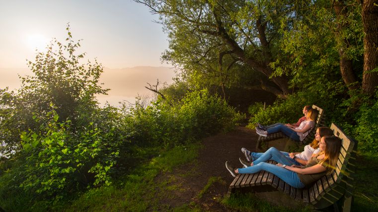 Je zwei Personen auf zwei Traumliegen beim Anschauen des Sonnenuntergangs am See