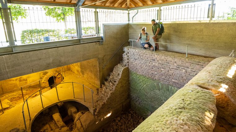 Two people look at an ancient Roman well room in a covered area.