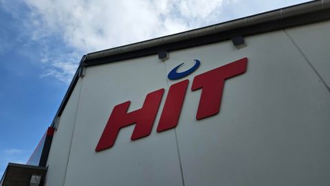Une partie d'un bâtiment avec le logo rouge "HIT". Le ciel à l'arrière-plan est partiellement nuageux.