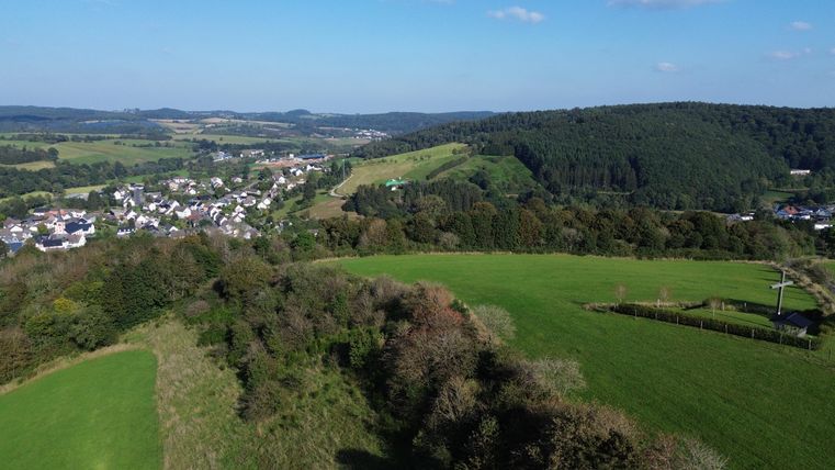 View from above of wide meadow and forest landscape with the village of Stadtkyll in the valley in between.