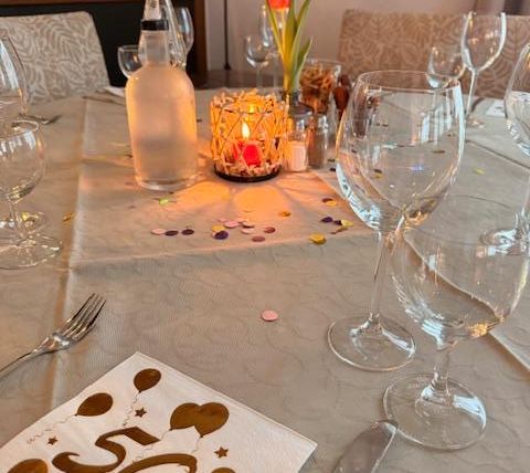 A festively set table for a 50th birthday. There are glasses, a candle, and a tablecloth with confetti and a "50th" napkin.