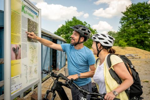 Two cyclists with helmets look at an information board on the Kyll cycle path.