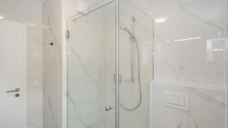 Eine moderne Dusche mit Glastüren und hellem, marmoriertem Fliesendesign. Der Raum wirkt sauber und elegant.