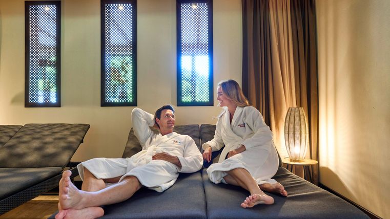 Un couple en peignoirs se détend dans un espace bien-être moderne. L'atmosphère est apaisante avec une lumière douce et un décor élégant.