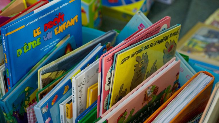 Eine Sammlung von bunten Kinderbüchern in verschiedenen Sprachen. Die Bücher sind auf einem Tisch gestapelt und vermitteln eine fröhliche Atmosphäre.