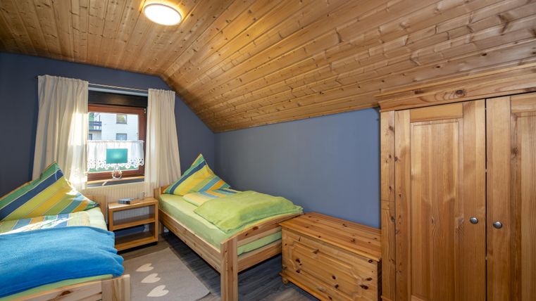 Een gezellig kamer met twee eenpersoonsbedden en houten wandbekleding. Helder gordijnen laten licht binnen, en een kast staat naast de bedden.