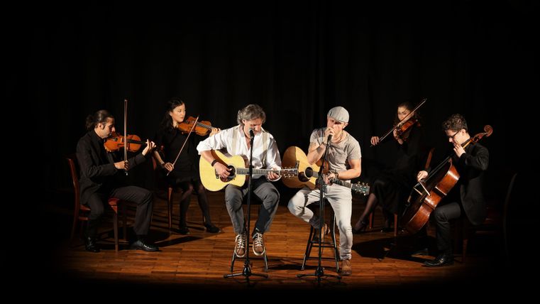 Simon u. Garfunkel mit Musikern im Hintergrund auf der Bühne