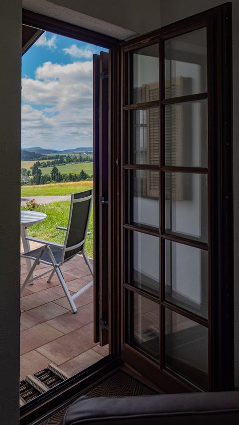 An open door overlooking a patio with a table and a chair. In the background, you can see green fields and a blue sky.