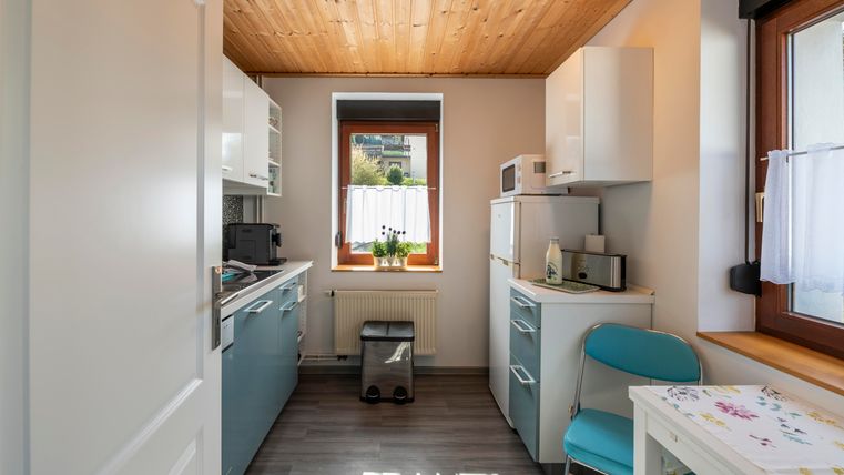 Een moderne keuken met een houten plafond en lichte muren. Op de tafel ligt een kleurrijke tafellaken en een stoel staat in de hoek geplaatst.