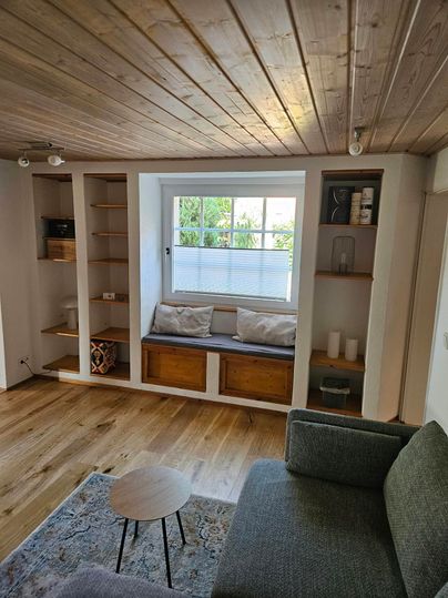 Een moderne woonruimte met een gezellige bank en een kleine tafel. De ruimte heeft lichte muren en een groot raam dat veel licht binnenlaat.