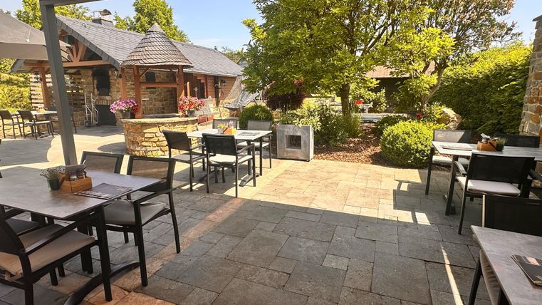 Een uitnodigend terras met tafels en stoelen. Omringd door groene planten en een gezellige sfeer.