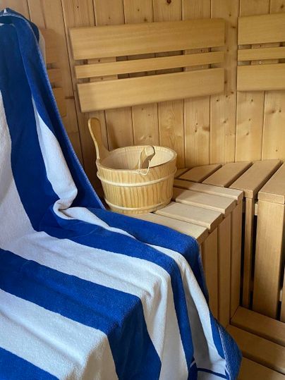 Une sauna confortable avec un banc en bois et une sélection de serviettes tissées à la main. Dans la pièce se trouve un seau en bois, placé sur le banc.