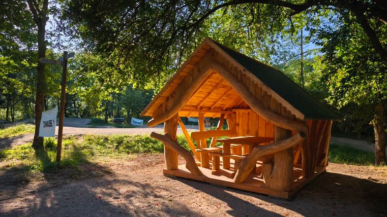 Une charmante cabane en bois se trouve dans la verdure, entourée d'arbres. Elle dispose d'un coin salon couvert et paraît accueillante.