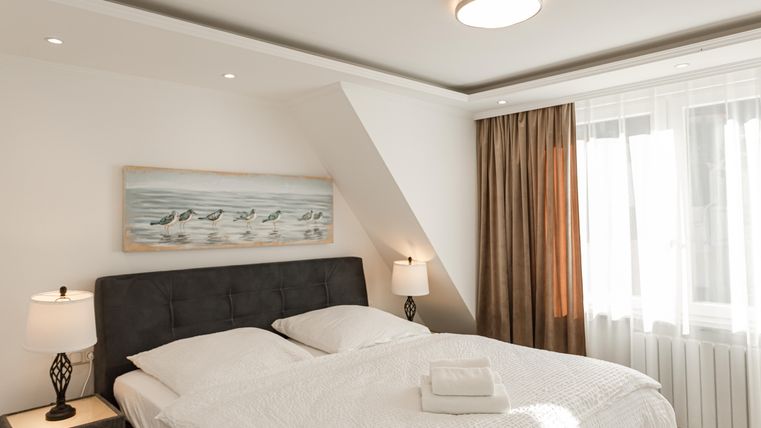 A cozy bedroom with a large double bed and two nightstands. Bright colors and windows with curtains create a relaxed atmosphere.