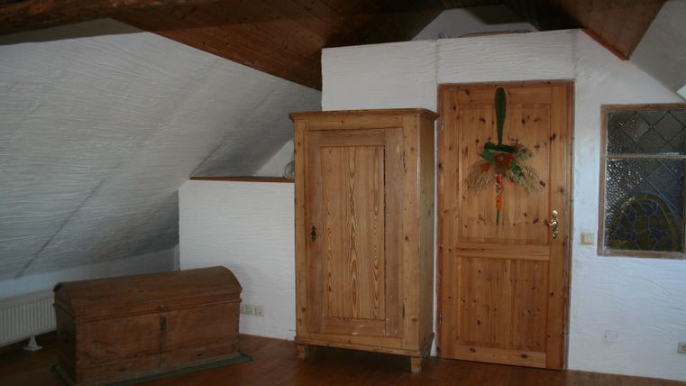 Een gezellige kamer met houten balken en schuine daken. Twee houten kasten staan tegen de muur, de vloer is van hout.