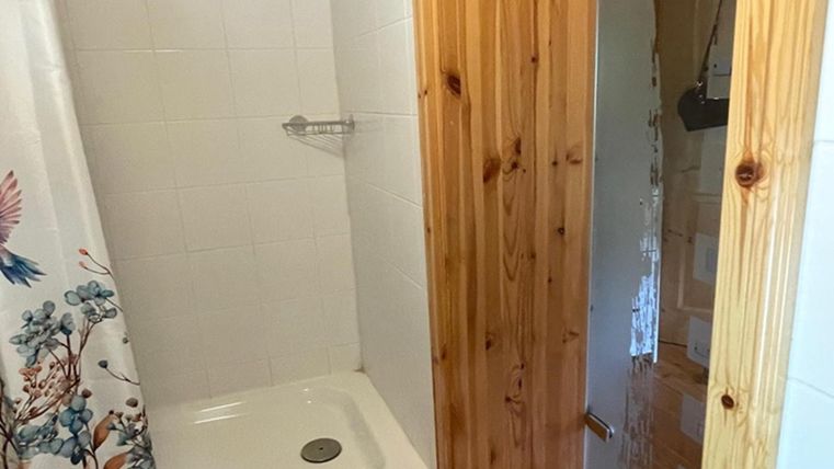 A simple shower with white tiles and a wood-paneled entrance area. The shower curtain features a floral design.