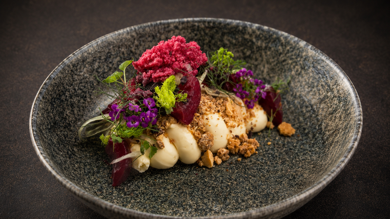 Een kunstzinnig opgemaakt bord met een dessertcreatie. De componenten zijn versierd met eetbare bloemen en een kleurrijke textuur.