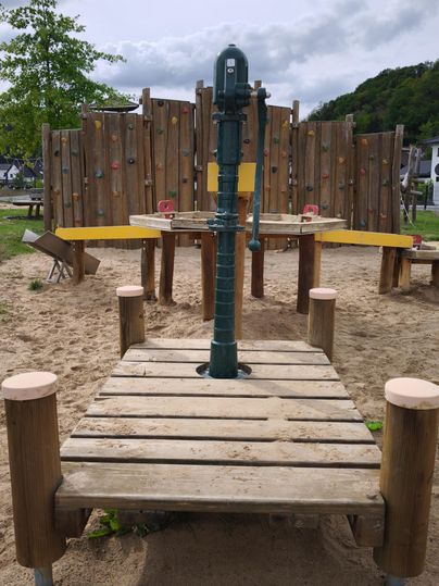 Een speeltuin met een waterpomp in het midden. Op de achtergrond zijn klimwanden en een zandbak te zien.
