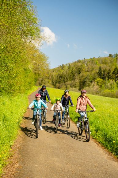 Eltern und drei Kinder fahren Rad auf einem asphaltierten Weg