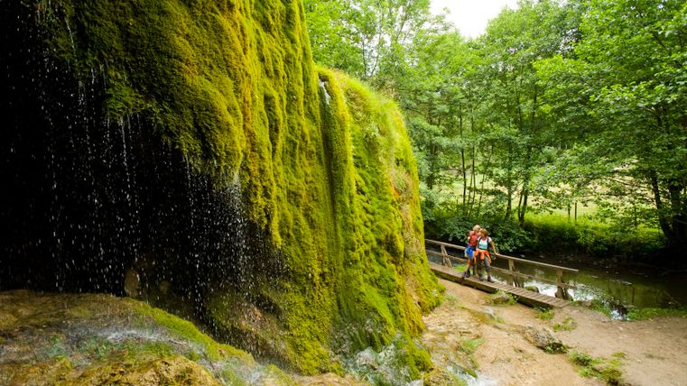 Nohn waterval met met mos bedekte rotsen en twee mensen op een loopbrug.