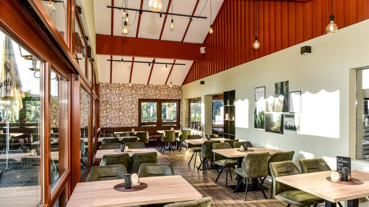 A cozy restaurant with large windows and wood paneling. The tables are set up in a modern style with comfortable chairs.