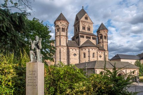 Une église impressionnante avec des tours marquantes et un bâtiment en pierre historique. Au premier plan, il y a une statue qui attire l'attention sur les environs.