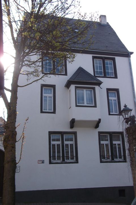 A three-story, white building with a pointed roof. It has several windows and is next to a tree.