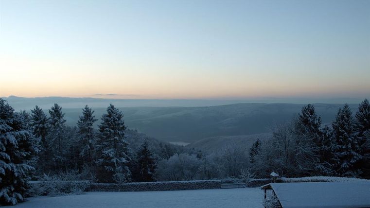 Un paysage d'hiver avec des arbres enneigés et des collines douces. Le ciel a un beau dégradé de couleurs aux premières heures du matin.