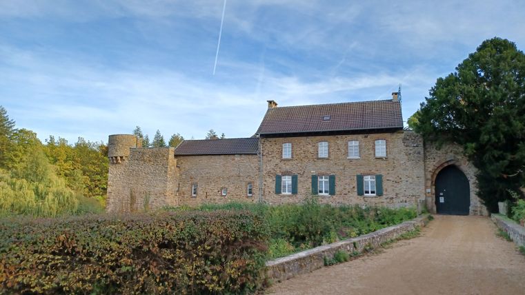 Uitzicht op kasteel Hardtburg met stenen muren en een boog, omringd door bomen en een heldere hemel.