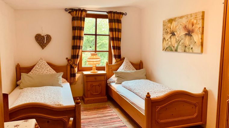 Een gezellige kamer met twee eenpersoonsbedden en een houten stoel. Grote ramen met gele gordijnen en een mooie bloemenschilderij aan de muur.