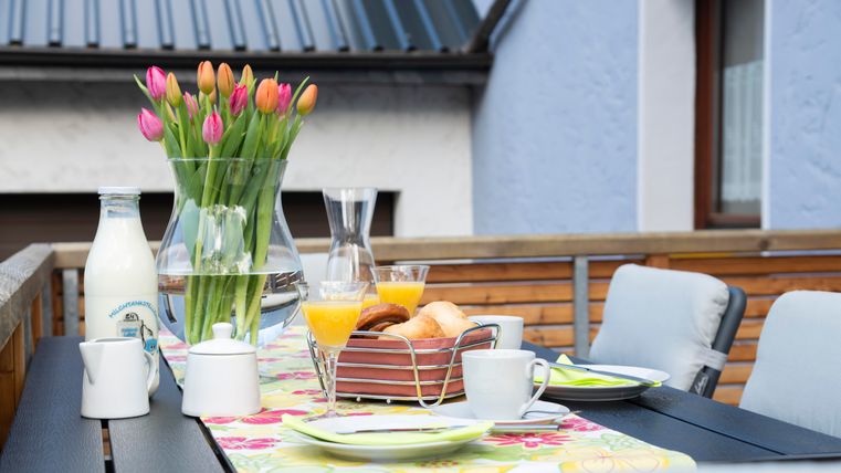 Een mooi gedekte tafel op een terras met verse bloemen, melk en ontbijt lekkernijen. De sfeer is uitnodigend en perfect voor een ontspannen ochtend.