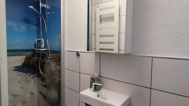 De linkerkant van de moderne badkamer met een douchecabine en een spiegel. De muur toont een mooi motief van een strand.