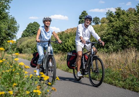 Frau und Mann fahren Fahrrad auf einem Radweg, sie haben Gepäcktaschen dabei