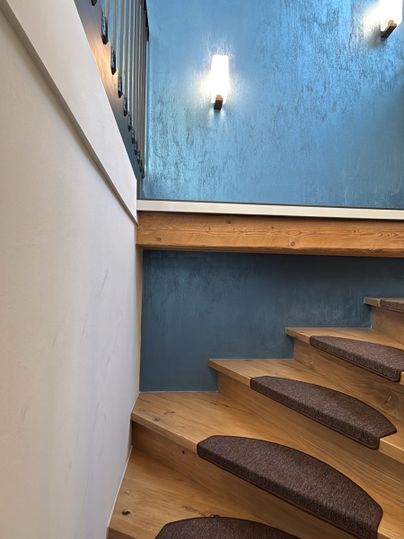 A modern wooden staircase with padded steps. The walls are painted in a stylish blue, and the lighting creates a pleasant atmosphere.