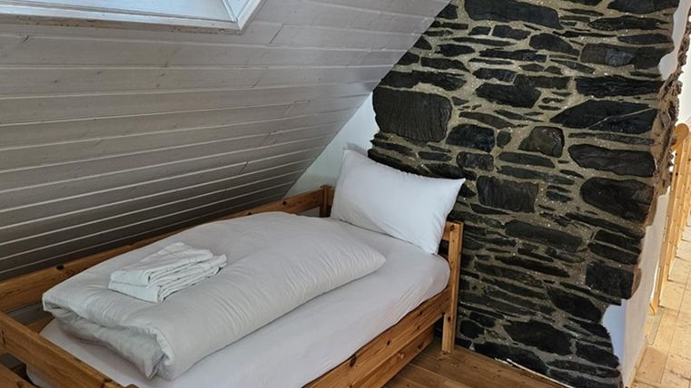 Een gezellige slaapkamer met een houten bed en frisse handdoeken. De muren zijn gedeeltelijk bekleed met natuursteen, wat een rustieke charme geeft.
