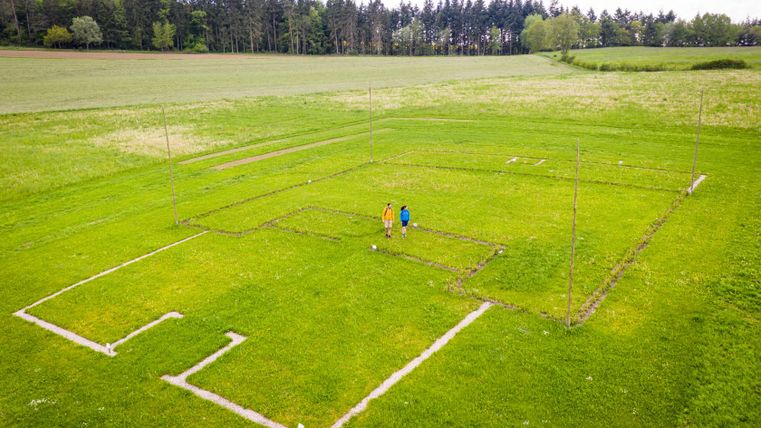 Luchtfoto van twee mensen op een veld met gemarkeerde plattegronden van een Romeinse villa.