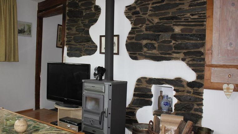 Een gezellige woonruimte met een moderne kachel en een televisie. De muren zijn versierd met natuurlijke stenen, wat een rustieke sfeer creëert.