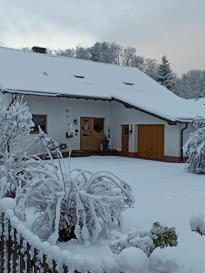 Een besneeuwd huis in een winterlandschap. De tuin en het hek zijn ook bedekt met een dikke laag sneeuw.