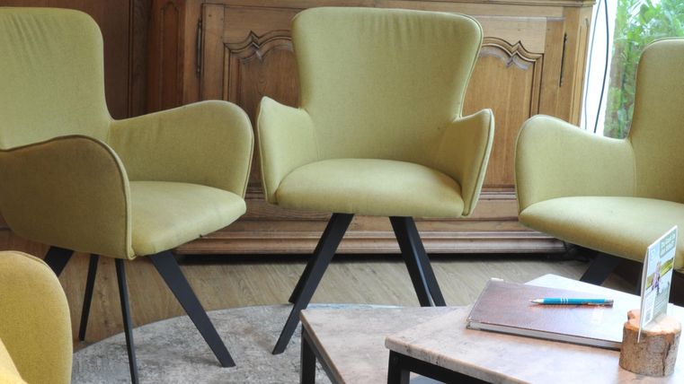 Ein gemütlicher Sitzbereich mit vier gelben Stühlen und einem Holztisch. Im Hintergrund steht ein antik aussehender Schrank.