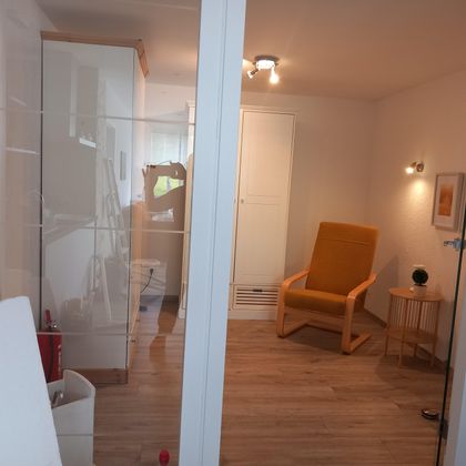 Een lichte kamer met modern design. Een oranje bureaustoel staat naast een kleine tafel en een decoratief accessoire.