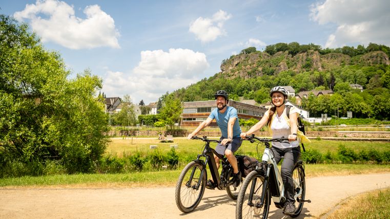 Two people riding bicycles on a path in the Gerolstein spa gardens. Trees and a hill can be seen in the background.