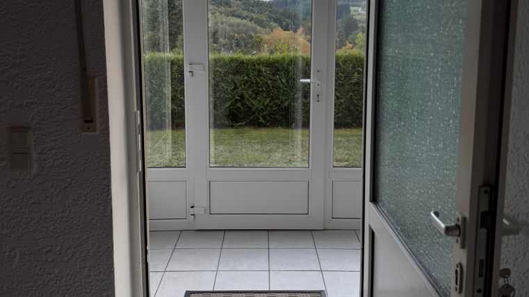 A bright entrance area with tiled flooring and a doormat.
Through large windows, view of a green landscape.