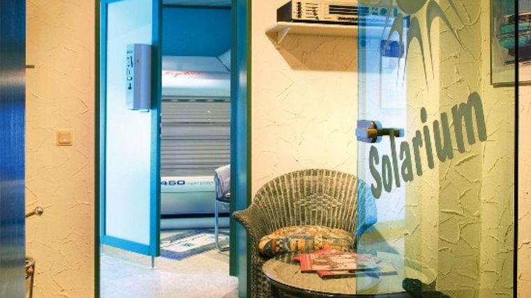 Een lichte kamer met toegang tot een solarium. Er staat een stoel en tijdschriften op een tafel.