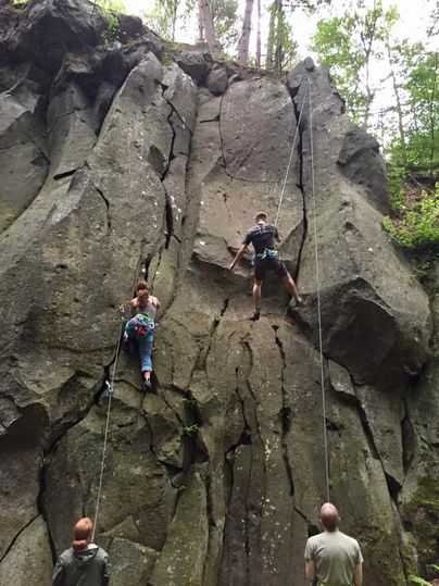 Een groep mensen klimt aan een steile rotswand. Twee klimmers zijn actief, terwijl andere mensen van onderen toekijken.