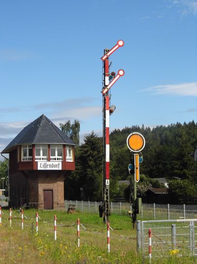 An old signal box building with the inscription 'Lissendorf' and a mechanical railroad signal against a blue sky.